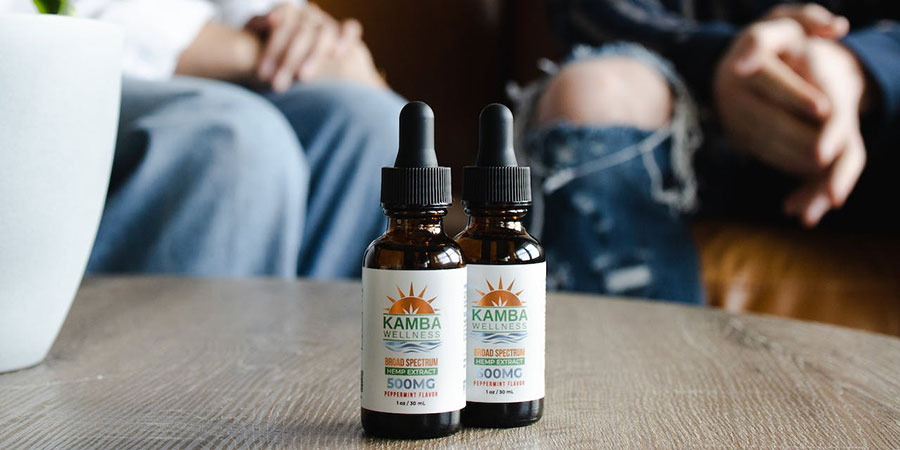 close up view of two bottles of hemp extract on top of a table and two people sitting on a couch in the background