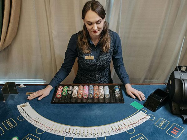 a woman as a dealer standing behind a casino table with playing cards spread on top of it